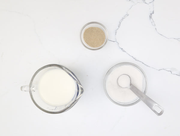 Ingredients for pear and caramel brioche buns: milk, yeast and sugar laid out on the counter