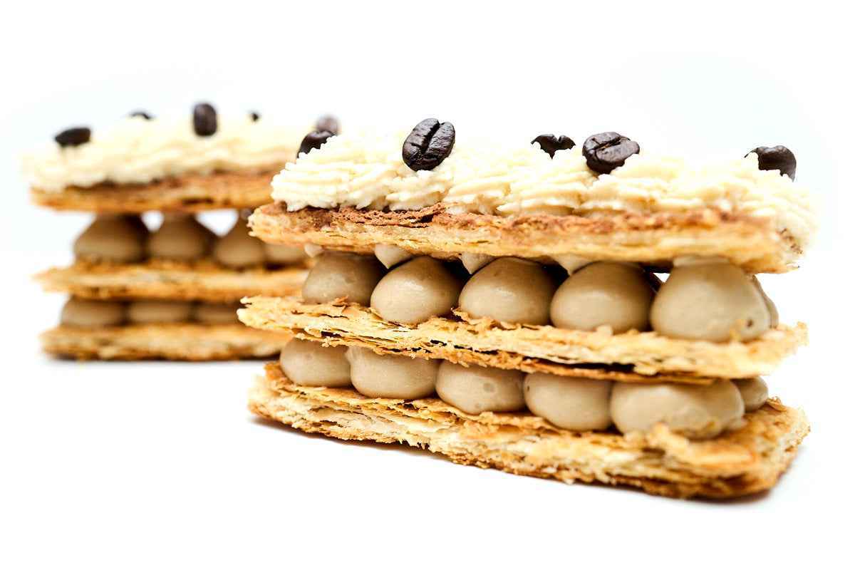 Tiramisu Napoleons: espresso pastry cream between crispy puff layers, topped with cream and coffee beans.