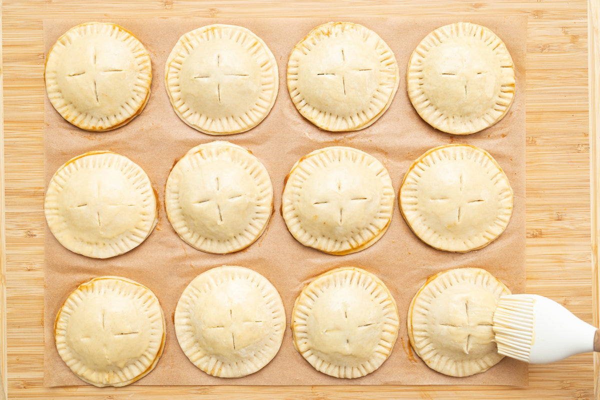 Brushing egg wash over the hand pies before baking