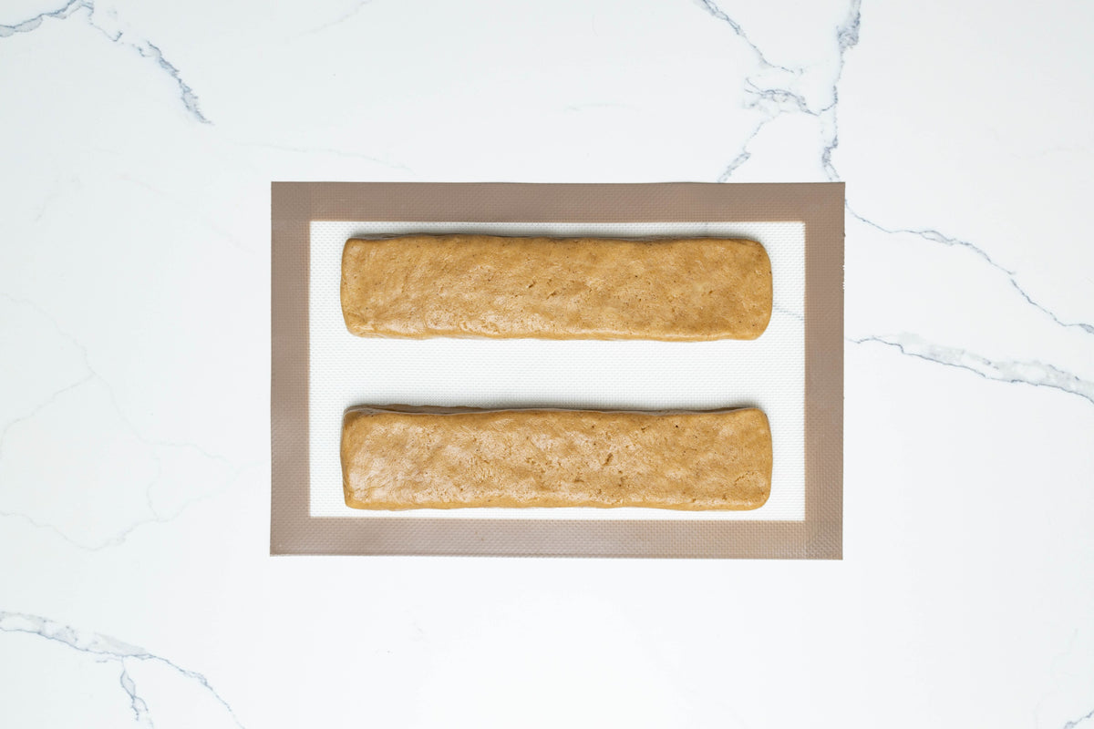 Biscotti dough shaped into two logs on a baking mat