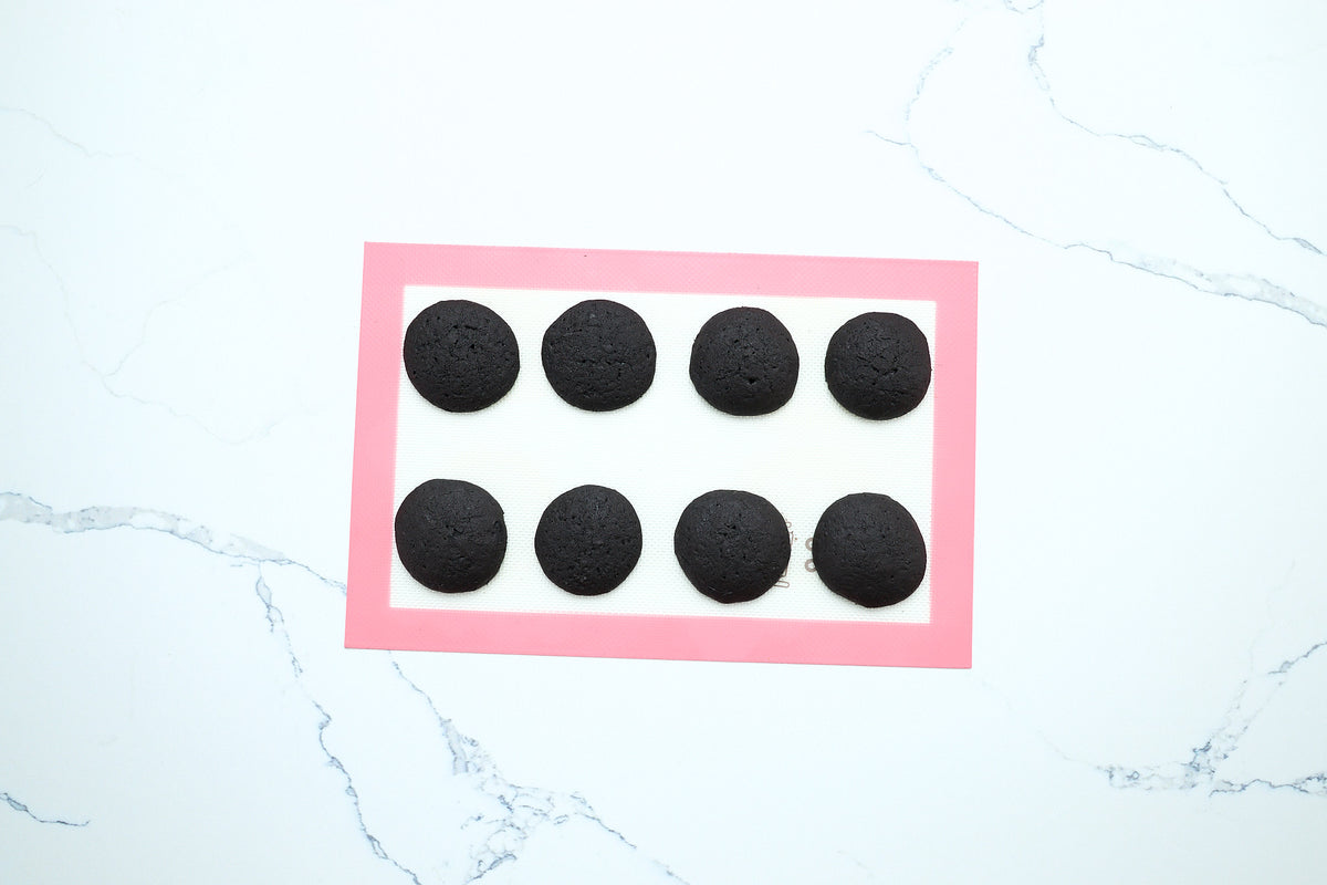 Baked dark chocolate whoopie pie cakes on a baking mat