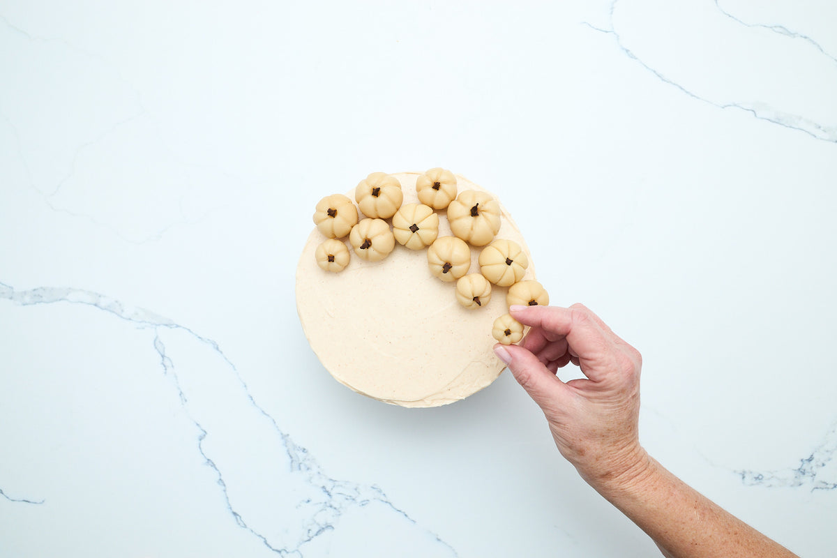 Placing marzipan pumpkins on top of the frosted cake