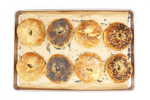 Assorted bagels on a baking tray with a white background