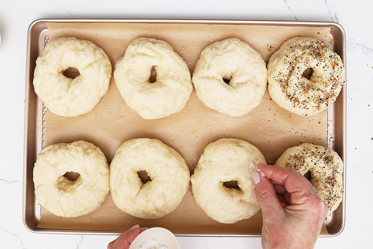 Hand sprinkling seasoning on homemade New York style bagels before baking in a gourmet baking kit