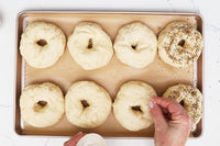 Hand sprinkling seasoning on homemade New York style bagels before baking in a gourmet baking kit