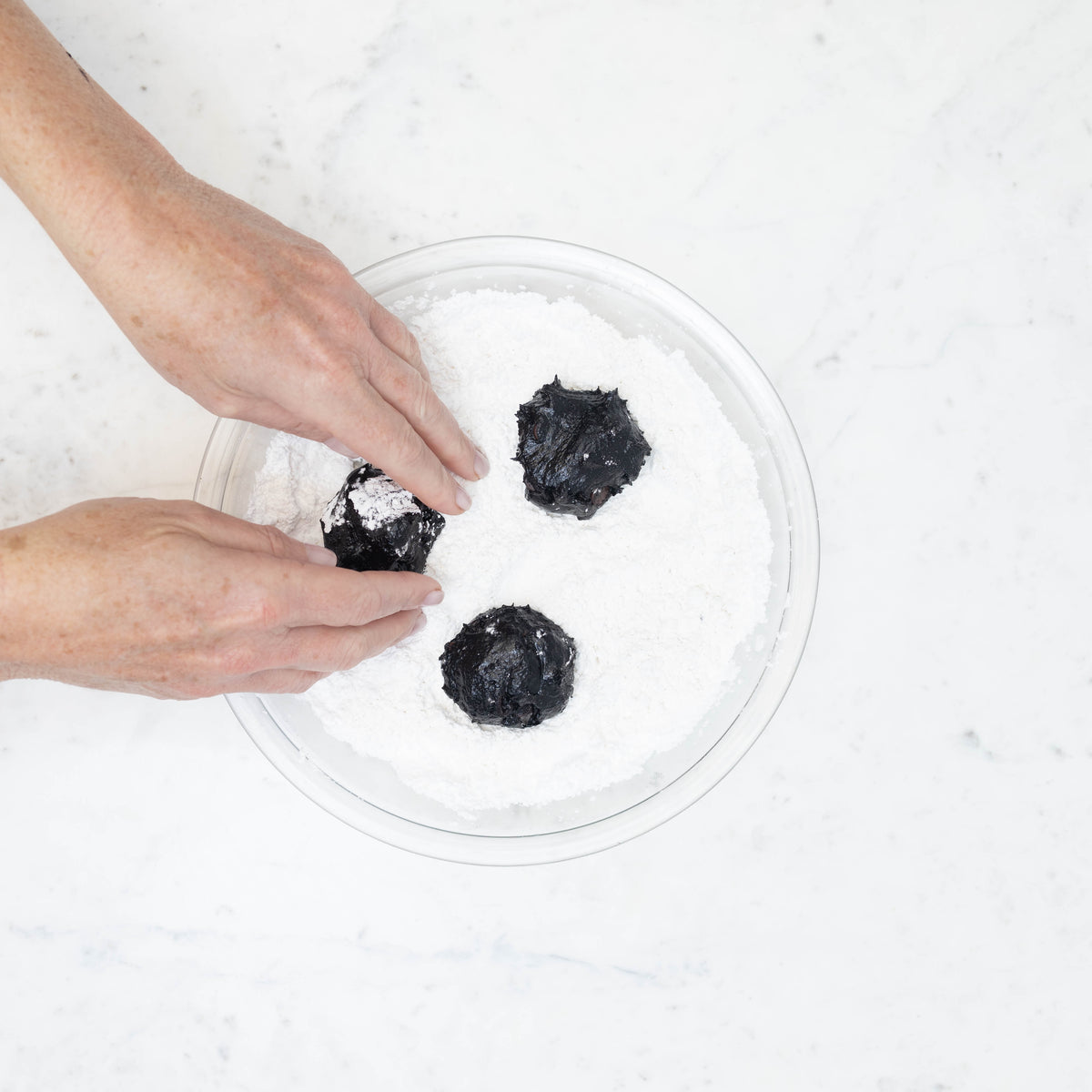 Rolling cookie dough balls in powdered sugar to create the crinkle finish