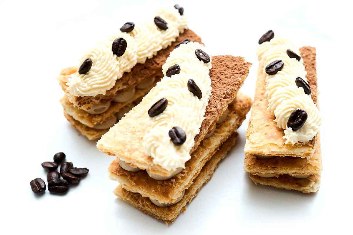 Tiramisu Napoleons: espresso pastry cream between crispy puff layers, topped with piped cream and coffee beans.